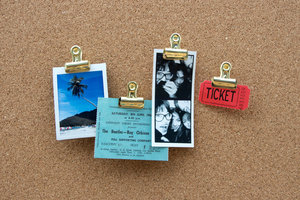 gold push pins on a cork pin board with tickets and photos