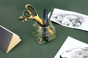 Giant glass inkwell pencil pot on a desk with ink drawings