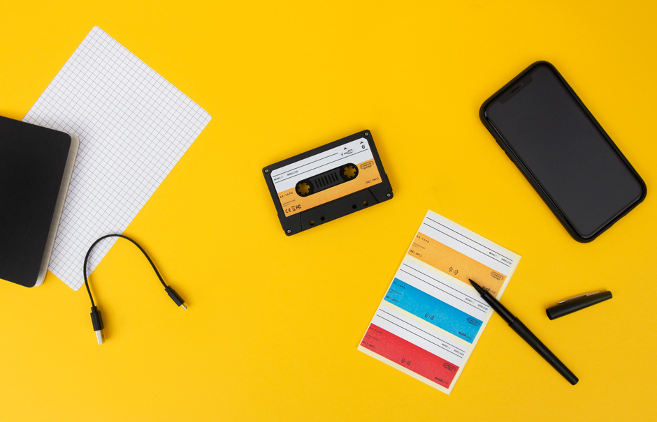 Cassette tape speaker on yellow desk with phone, stickers and charging cable