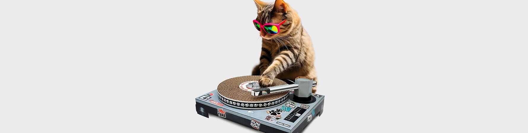 Tabby cat wearing pink sunglasses playing with a cardboard DJ turntable - the Suck UK Cat Scratch Turntable gift for cats.