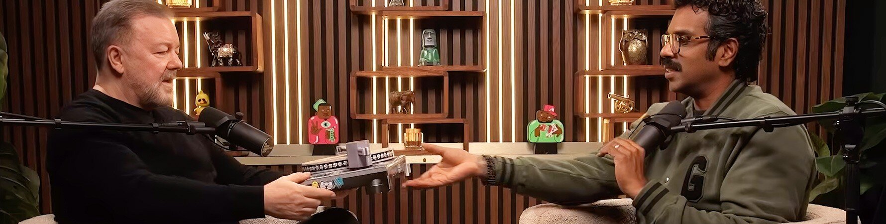 Romesh Ranganathan handing Ricky Gervais the Cat Scratch Turntable gift during The Romesh Ranganathan Show