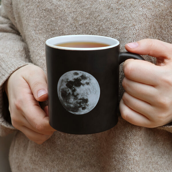 someone holding a black moon mug with tea  nasa space photography